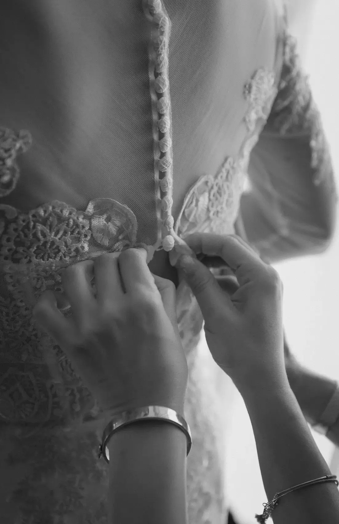 Bridesmaid's hands fastening the covered buttons on the back of a lace wedding dress
