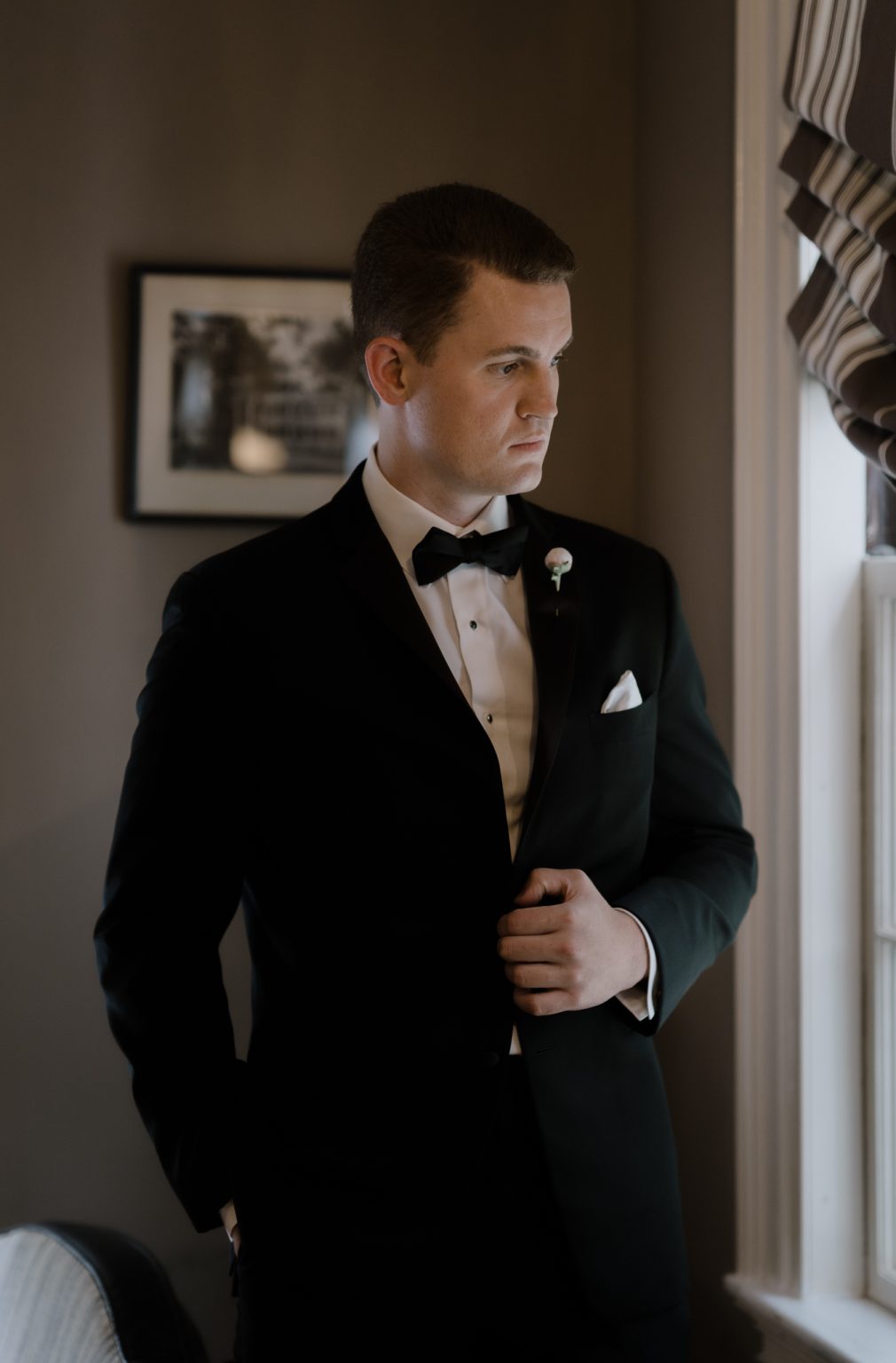 Groom adjusting his jacket in soft window light before the ceremony at Glen magna Farms