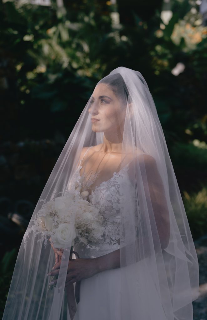 Bride in a cathedral veil holding her bouquet in a garden setting.