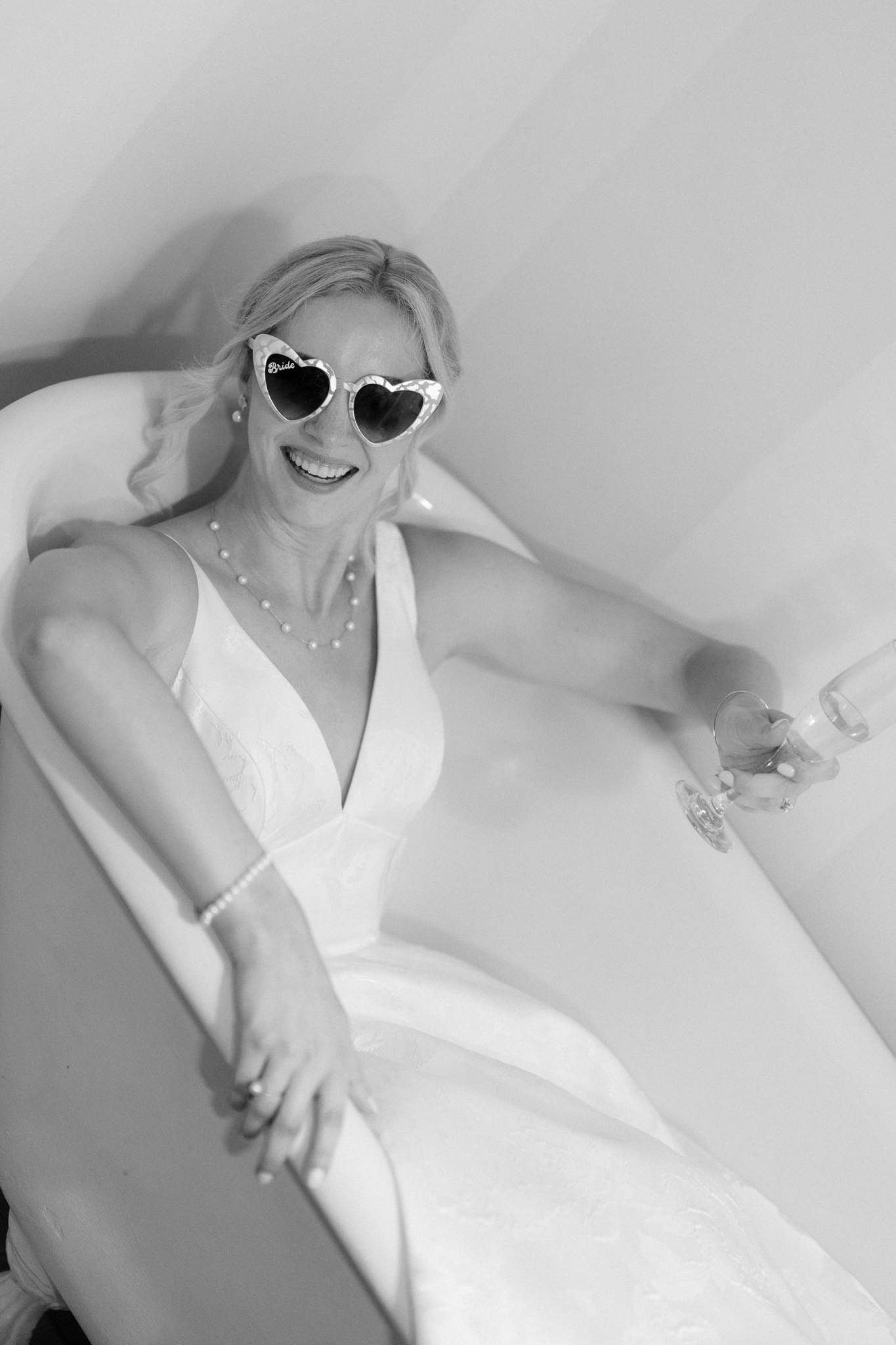 Bride posing in a bathtub wearing sunglasses, celebrating the end of her wedding reception at Glen Magna Farms, Danvers, MA