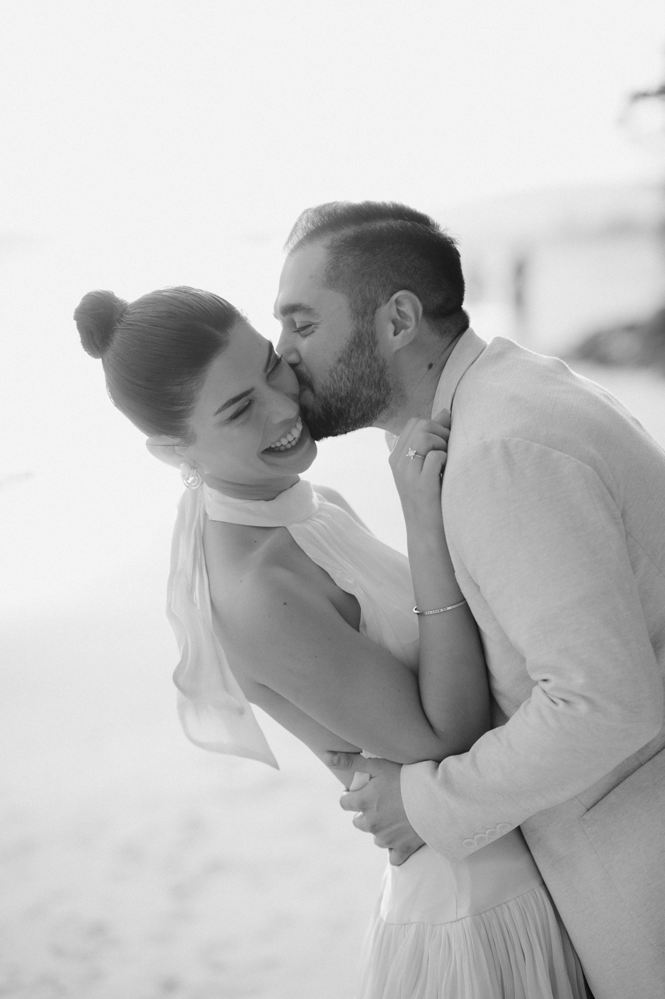 Candid wedding portrait on the beach where the groom is smothering the bride with kisses to the cheek.