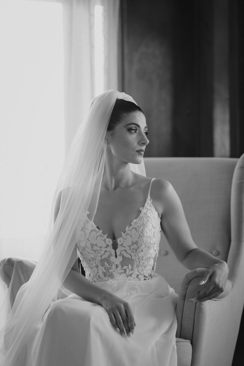 Bride in a long veil seated by a window before her wedding