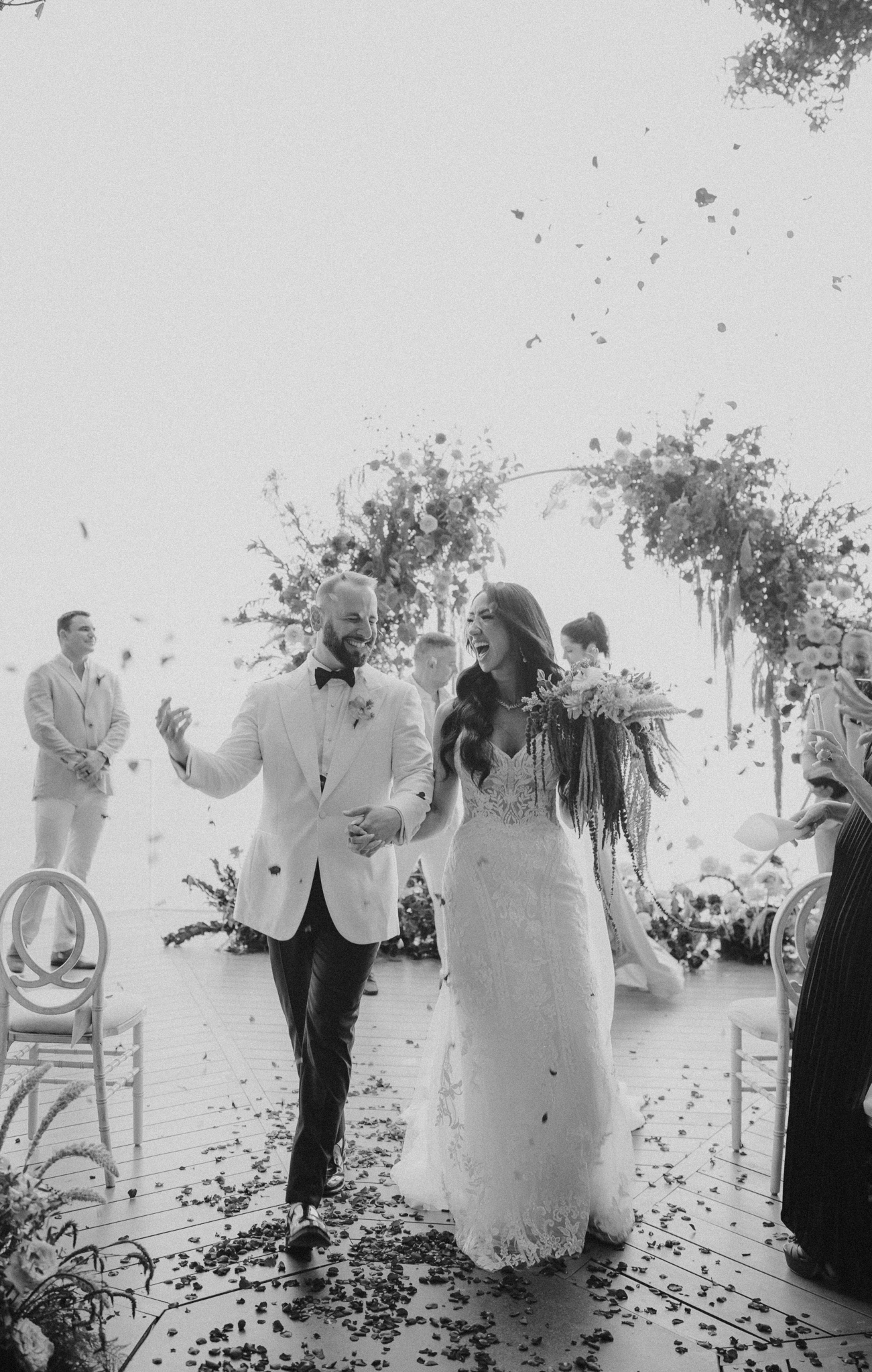 Newlyweds walking back down the aisle as guests toss petals, black and white ceremony exit